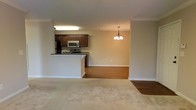 This single-floor residence offers a thoughtfully designed open-concept layout that connects the main living areas into one cohesive and functional environment. The kitchen is outfitted with dark espresso cabinetry, a stainless steel appliance suite including a refrigerator, microwave, and electric range, and a raised peninsula that provides a natural divide between the kitchen and the rest of the living space. The peninsula also offers casual seating potential, making it ideal for everyday dining or entertaining. Crown molding runs along the ceiling throughout, adding a refined architectural detail to the interior. Adjacent to the kitchen, the dining area is distinguished by warm hardwood-style flooring and is anchored by an elegant chandelier that adds a touch of classic charm. The living room flows naturally from the dining space and features neutral-toned carpeting, creating a comfortable and inviting atmosphere. The warm beige walls and consistent trim work throughout contribute to a clean, cohesive aesthetic. The open design ensures easy movement between all areas, making the space feel airy and well-proportioned. Overall, this home balances practical functionality with tasteful design elements suited for comfortable everyday living.