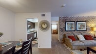 This single-floor residence is defined by a thoughtful layout that connects the living, dining, and kitchen areas in a cohesive, open arrangement. The living room serves as the focal point of the home, highlighted by a striking full-height exposed brick accent wall that adds warmth and character to the space. Plush carpeting runs throughout, complementing the neutral wall tones and creating a cozy atmosphere. A large window allows natural light to fill the room, enhancing its inviting feel.

The dining area is positioned adjacent to the living space and kitchen, offering convenient flow for everyday living and entertaining. It comfortably accommodates a full dining set and features a double-door closet for additional storage. A framed art piece adorns the wall, adding a decorative touch.

The kitchen features dark cabinetry with ample storage, a double sink, and tile flooring that contrasts the carpeted common areas. It is efficiently laid out with good counter space and appliances integrated throughout.

The bedroom is generously proportioned, featuring soft carpeting, dual closets, and a window dressed with sheer curtains that diffuse natural light. The room comfortably fits a full bedroom suite, offering both functionality and a restful ambiance throughout.