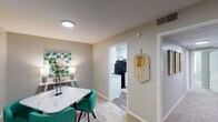 This single-story residence offers a thoughtfully arranged floor plan that balances comfort and functionality across its key living areas. The living room is generously proportioned, finished with soft carpeting and neutral walls that create a bright, welcoming atmosphere. A window allows natural light to filter in, enhancing the open feel of the space.

Adjacent to the living room, a dedicated dining area provides a defined space for meals, complete with a window overlooking the exterior and room for a full dining set. The kitchen features white cabinetry, granite-style countertops, a stainless steel sink, and black appliances including a full-size refrigerator and range, all set on wood-look flooring.

The unit includes two bedrooms, both carpeted and finished in soft, neutral tones. The primary bedroom is notably spacious, featuring a ceiling fan, sliding closet doors offering ample storage, and a wall-mounted television setup. The second bedroom is comfortably sized with a sage-green accent wall adding a distinct character.

The bathroom showcases granite countertops, a white undermount sink, white cabinetry, and classic subway tile wainscoting, lending a clean, polished aesthetic throughout.