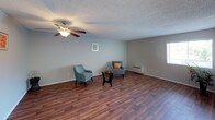 This single-floor residence offers a thoughtfully laid-out interior with a blend of practical finishes and comfortable living spaces. The main living area is anchored by rich wood-look flooring and neutral gray walls, with a ceiling fan overhead and a wall-mounted HVAC unit providing climate control. Natural light filters in through windows fitted with horizontal blinds, creating a bright and welcoming atmosphere. The open hallway connects the living space seamlessly to the rest of the unit.

The kitchen is well-equipped with white cabinetry, granite-style speckled countertops, a double-basin stainless steel sink, and a white electric range with an overhead exhaust hood. A window above the counter brings in additional natural light.

The bedrooms are finished with wall-to-wall carpet in warm neutral tones and textured ceilings. One bedroom features a sliding-door closet, while another offers a window with exterior views. Both rooms maintain a clean, understated aesthetic.

Two bathrooms serve the unit. One features a granite-style vanity counter, a large mirror with overhead lighting, a chrome towel ring, and a walk-in shower. The second bathroom includes a full tub-shower combination with a curtain rod, toilet, and matching countertop. Both bathrooms are finished in neutral tones with chrome fixtures throughout.