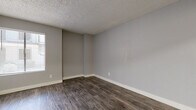 This single-floor unit offers a clean, modern aesthetic characterized by neutral gray walls, crisp white baseboards, and durable wood-style flooring that flows consistently throughout the space. The layout, as revealed by the 3D overview, includes an open living area, kitchen, multiple rooms, and a full bathroom, all thoughtfully arranged for functional everyday living.

The living and bedroom areas share a cohesive design language — textured popcorn ceilings, wide horizontal blinds that invite natural light, and generous wall space for flexible furnishing arrangements. A ceiling fan with a built-in light fixture provides both comfort and illumination in one of the rooms, which also features a closet with an exposed rack system.

The kitchen is efficiently designed with white cabinetry, light stone-look countertops, and stainless steel appliances including a range with a coil cooktop, oven, and refrigerator. A pantry closet with paneled bi-fold doors adds convenient storage. Light-toned wood-style flooring in the kitchen contrasts subtly with the deeper tones found in other areas of the unit.

The full bathroom is clean and functional, featuring a white vanity with a quartz-style countertop, a large mirror with modern lighting above, and a full tub-shower combination. Consistent wood-style flooring and gray wall tones tie the bathroom seamlessly into the overall design of the space.