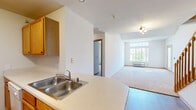 This two-floor residence offers a thoughtfully designed layout with functional living spaces spread across both levels. The kitchen is appointed with warm oak cabinetry, light countertops, a double stainless steel sink, white appliances including a range and refrigerator, and durable wood-look flooring. A dedicated walk-in pantry provides ample storage. The kitchen opens toward the living area, creating a connected, practical flow between spaces.

The living room is a standout area, featuring soaring vaulted ceilings and a large multi-pane window that fills the room with natural light and offers views of surrounding greenery. Plush neutral carpeting runs throughout the living spaces and bedrooms, adding warmth underfoot. A wall-mounted HVAC unit ensures year-round comfort.

The bedrooms are generously sized with soft carpet, warm wood baseboards, and windows that invite natural light. At least one bedroom includes a walk-in closet with built-in shelving and hanging rods, offering excellent storage capacity. Additional carpeted rooms provide flexible space for various uses.

The bathroom features a wide vanity with an integrated sink, clean white countertop, and a large mirror. Wood-trimmed doorways are consistent throughout, contributing to a cohesive interior aesthetic. The overall ambiance is clean, bright, and move-in ready.