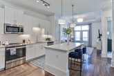 Located at 6000 Summit Pl in Alpharetta, Georgia, this thoughtfully designed single-floor residence combines refined aesthetics with functional living. The living room serves as the heart of the home, showcasing elegant wainscoting, hardwood floors, a statement chandelier, and French doors that invite abundant natural light and outdoor views. A large-scale abstract artwork anchors the space above a comfortable neutral sofa, creating a sophisticated yet inviting atmosphere.

The kitchen is both stylish and highly functional, featuring white shaker cabinetry, stainless steel appliances, a herringbone-pattern hardwood floor, a geometric tile backsplash, and a central island with built-in shelving — ideal for cooking and casual dining. Track lighting and pendant fixtures illuminate the space effectively.

The primary bedroom is generously proportioned, offering large windows with views of the surrounding community, plush carpeting, and ample natural light. A secondary bedroom provides a cozy retreat with soft neutral tones. The full bathroom features marble-style tile, a soaking tub, and a wide double-sink vanity. The walk-in closet is outfitted with a comprehensive wire shelving system, offering well-organized storage throughout.