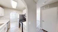 This single-floor residence offers a clean, modern aesthetic throughout, with light vinyl plank flooring, neutral gray walls, and textured ceilings that create a cohesive and welcoming atmosphere.

The kitchen is a functional highlight, accessed through a distinctive arched entryway and bathed in natural light from a skylight overhead. It features stainless steel appliances, including a gas range, over-the-range microwave, and refrigerator, complemented by crisp white cabinetry with brushed nickel hardware and bright white countertops.

The living area is generously proportioned and bathed in natural light, with a sliding glass door fitted with vertical blinds that opens to the outdoors. A ceiling fan adds comfort to this airy space, which flows naturally from the kitchen and dining areas.

The bedroom offers a tranquil retreat with a natural light-filled window, soft neutral tones, and direct access to a built-in shelved walk-in closet, providing ample storage.

The bathroom is clean and well-designed, featuring a full soaking tub and shower combination with tiled surround, a white vanity with under-cabinet storage, and a large mirror. Arched architectural details echo the design language found throughout the space, adding a touch of character to the otherwise contemporary interior.