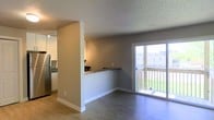 This well-appointed single-floor space offers a thoughtfully designed open-concept layout that effortlessly connects the kitchen and living areas. The kitchen is equipped with stainless steel appliances, including a full-sized refrigerator, and features a granite-topped breakfast bar that serves as both a functional workspace and a casual dining spot. Track lighting illuminates the kitchen, highlighting its modern finishes. The living area is finished with smooth hardwood-style flooring that extends throughout, creating a cohesive and easy-to-maintain surface underfoot. Neutral gray walls provide a versatile backdrop that complements a wide range of décor styles. A textured popcorn ceiling adds a classic touch overhead. A sliding glass door floods the living space with natural light and opens directly onto a private balcony, offering pleasant outdoor views of the surrounding landscape and neighboring buildings. The balcony features a classic railing and provides a comfortable outdoor retreat. Clean white baseboards and trim throughout add a crisp, polished finish to the overall aesthetic of this inviting, light-filled space.