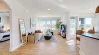 Located at Waters Edge Village in Charlotte, NC, this 2-bedroom, 3-bathroom single-floor residence offers a thoughtfully designed open-concept layout filled with natural light. The living room is anchored by a bank of large windows framing stunning waterfront views, with light wood flooring running seamlessly throughout the space and clean white walls creating an airy, modern atmosphere. The kitchen features white shaker cabinetry with gold hardware, dark stone countertops, a subway tile backsplash, and a central island with seating — all bathed in natural light from oversized windows. The dining area flows effortlessly between the kitchen and living spaces. The primary bedroom is a serene retreat with waterfront-facing windows, soft neutral tones, and access to a walk-in closet with ample shelving and hanging storage. Its en-suite bathroom includes a soaking tub and generous vanity. The second bedroom also benefits from water views and a ceiling fan. A dedicated closet and two additional hallways provide practical storage and connectivity throughout. Three full bathrooms ensure convenience for residents and guests alike. The consistent warm wood flooring, abundant natural light, and tranquil lakeside views lend the entire residence a calm, welcoming ambiance.