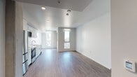 This thoughtfully designed single-floor unit offers a clean, contemporary aesthetic throughout. The open-concept living and kitchen area is anchored by smooth hardwood-style flooring and bright white walls, creating a light-filled, airy atmosphere. Large floor-to-ceiling windows frame sweeping urban skyline views, flooding the space with natural light and lending a sense of openness.

The kitchen is well-appointed with sleek, high-gloss white cabinetry extending to the ceiling for ample storage, light-toned quartz countertops, and a full suite of stainless steel appliances including a refrigerator, electric range, over-the-range microwave, and dishwasher. A undermount sink with a modern arc faucet completes the functional and stylish workspace.

The bedroom area is a quiet, minimalist retreat with clean white walls and continued hardwood-style flooring. The entry features a secure keypad-entry door alongside a utility panel, offering both convenience and functionality.

The bathroom is finished to a high standard, showcasing a marble-veined quartz vanity countertop with an undermount sink, a large frameless mirror, chrome fixtures, and a tiled shower-tub combination. The all-white palette enhances the sense of cleanliness and space. Overall, the unit presents a polished, move-in-ready environment suited to modern urban living.