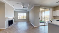 This well-appointed single-floor residence showcases a thoughtful layout and contemporary finishes throughout. The spacious living room serves as the heart of the home, featuring a striking tray ceiling with crown molding, a ceiling fan, a classic fireplace, and herringbone-patterned flooring that extends throughout the unit. A large window fills the room with natural light, while a sliding glass door provides direct access to a private balcony with open outdoor views. Decorative built-in wall niches add an architectural accent to the living and dining areas, lending the space a refined character.

The kitchen is outfitted with crisp white cabinetry, light quartz countertops, stainless steel appliances including a French door refrigerator and dishwasher, and a deep single-basin sink beneath a bright window. An adjacent utility room provides added convenience. The bathroom features a vanity with illuminated mirror, white cabinetry, and a full tiled soaking tub with shower combination. Bedrooms are generously sized with ceiling fans, herringbone flooring, and ample natural light from well-placed windows. The neutral warm-toned color palette throughout creates a clean, cohesive, and welcoming ambiance ideal for modern living.