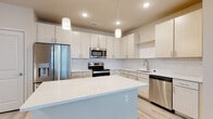 Located at 1155 Park Ln in Davenport, Florida, this single-story home presents a clean, modern aesthetic defined by a neutral color palette and light wood-style flooring that runs consistently throughout the space. The open-concept design seamlessly connects the kitchen and living areas, creating a sense of openness and ease of movement.

The kitchen serves as a central focal point, outfitted with light-toned cabinetry, a white subway tile backsplash, and quartz countertops. A generously sized island provides additional workspace and a natural gathering point. Stainless steel appliances, including a refrigerator with ice maker, range, microwave, and dishwasher, complete the well-appointed cooking space. Pendant lighting above the island adds a contemporary touch, while recessed lighting ensures thorough illumination throughout.

The bedrooms are bright and well-proportioned, each featuring ceiling fans and large windows with blinds that allow ample natural light. The bathrooms continue the home's modern aesthetic, with light cabinetry, quartz vanity surfaces, and clean tile work. The primary bathroom includes a glass-enclosed walk-in shower and a backlit vanity mirror, while the secondary bathroom offers a full soaking tub with tiled surround. The overall ambiance is bright, fresh, and move-in ready.