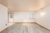 This single-floor residence offers a well-organized layout that balances open living with defined private spaces. The main living area makes a strong first impression with its gray wood-look laminate flooring, warm wood baseboards, and textured ceiling. Multiple windows fitted with horizontal blinds fill the space with natural light, and a front entry door with a sidelight window provides a welcoming point of arrival. Recessed lighting adds a clean, modern touch overhead.

The galley-style kitchen is efficiently designed with light maple cabinetry lining both sides, dark countertops, and a double-basin sink with a tile backsplash. Stainless steel appliances — including a refrigerator, electric range, over-the-range microwave, and dishwasher — complete the kitchen's functional setup. Light tile flooring runs throughout the kitchen and entry areas.

The bedrooms are carpeted for comfort and each feature windows with garden views and baseboard heating units, ensuring year-round warmth. The bathroom is clean and straightforward, offering a full tub-shower combination, a toilet, a single-sink vanity with a wood cabinet, and tile flooring. A hallway connects the living spaces to the private rooms, with warm wood-toned trim providing visual continuity throughout the home.