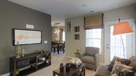 This two-floor residence offers a thoughtfully designed interior that blends contemporary style with comfortable, everyday functionality. The living area serves as the heart of the main floor, featuring warm neutral walls accented by a bold dark gray feature wall that adds depth and visual contrast. Soft carpeting underfoot contributes to the relaxed ambiance, while a large window dressed with a tailored Roman shade allows natural light to fill the space. Decorative wall art and carefully curated furnishings, including a cushioned armchair and a dark wood coffee table, complete the inviting atmosphere.

The living space flows naturally into the dining area, which is visible through an open passageway. The dining room accommodates a full table and chair set beneath a modern cluster pendant light fixture, adding a refined focal point overhead. A secondary window in the dining area introduces additional natural light. The neutral color palette carries throughout, creating a cohesive and harmonious feel. Together, the spaces reflect a well-considered layout that balances open connectivity with distinct functional zones across multiple levels.