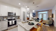 This single-floor residence showcases a thoughtfully designed open-concept layout where the kitchen flows seamlessly into the living area. The kitchen is a standout feature, equipped with stainless steel appliances including a side-by-side refrigerator, electric range, and built-in microwave. White cabinetry with ample storage pairs elegantly with granite countertops, a subway tile backsplash, and a central island that doubles as a breakfast bar with pendant globe lighting overhead. Wood-look flooring runs throughout the main living areas, adding warmth to the bright, white interior.

The living room exudes character with an exposed brick accent wall framing a set of French doors that invite natural light and outdoor views. The space is cozy yet open, offering a welcoming retreat.

Two bedrooms provide comfortable accommodations, each with plush carpeting and large windows. The primary bedroom connects to a private en-suite bathroom featuring a walk-in glass shower, granite vanity, and wood-look flooring. A second full bathroom offers a soaking tub and shower combination with a matching granite vanity, serving the secondary bedroom with equal attention to detail. Clean white walls and gray-toned cabinetry throughout create a cohesive, modern aesthetic.