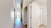 This thoughtfully designed unit in Lakewood, Colorado, makes efficient use of its space with a clean, modern aesthetic throughout. The open-concept kitchen and living area serves as the heart of the unit, featuring warm wood-toned lower cabinetry, crisp white upper cabinets, a tile backsplash, and stainless steel appliances including a range, microwave, and refrigerator. A large sliding glass door floods the space with natural light and provides direct access to a private balcony with exterior views. Durable wood-look flooring runs throughout, lending warmth and visual continuity across all areas. The hallway connects the main living space to the additional rooms and includes a sliding-door closet with a rod and shelf for organized storage, as well as a dedicated nook housing a stacked in-unit washer and dryer — a highly practical feature. A separate bedroom area offers a quiet, neutral retreat with light-toned flooring and clean white walls. The bathroom is finished with light-toned tile flooring, a warm wood vanity with a white countertop and integrated sink, a standard toilet, a grab bar, and a glass-door shower enclosure. Recessed lighting in the hallway and a ceiling fan in the main living area add functional comfort to this well-appointed Lakewood residence.