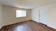 This single-floor residential unit offers a practical and comfortable layout with a variety of notable design details throughout. The living area welcomes you with durable wood-look flooring and neutral walls that create a bright, open feel. A standout architectural feature is the exposed brick wall that adds warmth and character, visible both in the living space and adjacent kitchen area. Natural light filters in through windows fitted with vertical blinds, offering views of surrounding greenery.

The kitchen is efficiently designed with cream-toned cabinetry, a white tile backsplash, and ample counter space. It is equipped with a gas range and a refrigerator, making it fully functional for everyday cooking. The wood-look flooring continues seamlessly into this space, and a ceiling-mounted light fixture provides overhead illumination.

The bedroom features soft, neutral carpeting underfoot and a large window that allows generous natural light while maintaining privacy through vertical blinds. The room's clean, open layout offers flexibility for furnishing.

The bathroom is well-appointed with a wood-toned vanity, granite-style countertop, a large wall mirror, and built-in medicine cabinet storage. Tile flooring and white-painted walls give the space a clean, functional aesthetic. Overall, the unit presents a cohesive and inviting living environment.