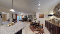 This single-floor residence offers a cohesive, open-concept layout that connects the kitchen, dining, and living areas into one continuous, functional space. The kitchen is designed in a galley configuration, featuring rich dark-espresso cabinetry extending to the ceiling, granite countertops, black appliances, and hardwood-style flooring. A breakfast bar with seating bridges the kitchen to the dining area, which accommodates a round dining table set atop a patterned area rug.

The living room is carpeted and finished with crown molding, a ceiling fan, and track lighting. French doors allow natural light to filter in and provide outdoor access, enhancing the open feel of the space. A dedicated media and seating nook adjacent to the living area offers additional flexible use.

Both bedrooms are carpeted and generously proportioned. The primary bedroom includes a walk-in closet with built-in shelving, providing well-organized storage. Each bathroom is finished with granite-topped dark vanities, hardwood-style flooring, and a tub-shower combination, maintaining a consistent design palette throughout. The overall ambiance is warm and cohesive, with neutral tones complemented by rich wood finishes.