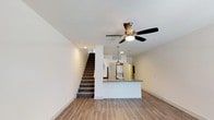 This two-story townhome at Greenview Towns, located at 1384 N. Clinton Ave. in Bay Shore, NY, offers a well-designed layout spread across two floors. The main level features an open-concept living area with wood-look plank flooring, recessed lighting, and a ceiling fan. A peninsula-style kitchen counter visually separates the living space from the kitchen, which is equipped with stainless steel appliances—including a gas range, over-the-range microwave, and refrigerator—paired with white shaker-style cabinetry and neutral countertops. Pendant lighting above the peninsula adds a polished finishing touch. A half bathroom on the main level features wood-look flooring and clean, white fixtures. A carpeted staircase leads to the upper floor, where a hallway with plush gray carpeting connects the bedrooms. The bedrooms feature ceiling fans, wood-look or carpeted flooring, and windows that bring in natural light. One bedroom includes a walk-in closet. The full bathroom upstairs is fitted with a tub-shower combination, white subway tile surround, and chrome fixtures, maintaining the home's consistent, modern aesthetic throughout.