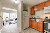 This single-floor studio unit at Kings Reserve in Memphis, Tennessee, offers a thoughtfully organized layout that maximizes its compact footprint. The main living area features warm hardwood-style flooring and neutral cream-toned walls that contribute to a bright, open atmosphere. Large windows with horizontal blinds line one wall, allowing generous natural light to fill the space while offering views of surrounding greenery. The room comfortably accommodates both sleeping and sitting areas, with enough space for a desk, making it well-suited for work-from-home use.

The combined kitchen and living room transitions seamlessly into the kitchen area, which is outfitted with rich warm-toned cabinetry, granite-style countertops, a stainless steel electric range, an over-the-range microwave, and a full-size refrigerator. Tile flooring in the kitchen provides a practical contrast to the living area's hardwood-style surface.

The bathroom features tile flooring, a walk-in shower with a curtain enclosure, and accessibility-friendly grab bars, reflecting a practical and inclusive design. A hallway with additional doors connects the main living space to the bathroom and entry, providing a sense of separation within the open layout.