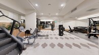 This expansive fitness room spans 1790 square feet on a single floor, offering a comprehensive workout experience. The space is intelligently designed with distinct zones for various exercise types. A row of cardio machines, including treadmills and ellipticals, lines one side of the room, facing large windows that likely provide natural light during daytime hours.

The central area is dedicated to strength training, featuring a diverse selection of weight machines and free weights. A multi-functional cable machine stands prominently, allowing for a wide range of exercises. Complementing this are several bench press stations and a squat rack for serious lifters.

The room's aesthetic is clean and modern, with white walls and ceilings brightened by recessed lighting and pendant fixtures. The flooring combines practical, cushioned surfaces with an attractive geometric pattern in neutral tones. Large mirrors line the walls, enhancing the sense of space and allowing users to monitor their form.

Thoughtful touches include wooden planter boxes with greenery, adding a natural element to the environment. The layout promotes easy navigation between equipment, with clear pathways and well-organized stations. Overall, this fitness room provides a professional-grade workout space with attention to both functionality and design.