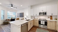 This thoughtfully designed single-floor residence showcases a clean, modern aesthetic with high-quality finishes throughout. The open-concept kitchen is a standout feature, equipped with stainless steel appliances including a French door refrigerator, gas range, built-in microwave, and dishwasher. Cabinetry combines crisp white upper cabinets with warm natural wood lower cabinets, accented by matte black hardware and a classic white subway tile backsplash. A peninsula with a quartz countertop and undermount sink provides additional prep space and connects seamlessly to the living area.

The living room is bright and welcoming, featuring durable hardwood-style flooring, recessed lighting, and large windows fitted with horizontal blinds that allow for ample natural light. The space flows naturally from the kitchen, making it ideal for entertaining.

Two bedrooms offer comfortable retreats, each with plush carpeting and windows that bring in natural light. The rooms are well-proportioned, providing a calm and restful atmosphere.

The bathroom is finished with light tile flooring, a natural wood vanity with a white countertop, matte black fixtures, and a bright vanity mirror with contemporary lighting above. Clean white walls and panel-style doors complete the polished look throughout this well-appointed residence.