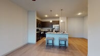 This single-story unit in Buda, Texas, presents a well-designed open-concept layout with consistent wood-look flooring and neutral gray-toned walls throughout. The kitchen serves as a central focal point, outfitted with rich dark espresso cabinetry, granite-style countertops, and a full suite of stainless steel appliances including a range, microwave, and French door refrigerator. A kitchen island with a built-in sink and seating for two is highlighted by pendant lighting above, creating a functional and inviting space that flows seamlessly into the living area, which features a ceiling fan and natural light from a nearby window.

The bedrooms are generously proportioned, each equipped with ceiling fans and wood-look flooring. Notable among them are walk-in closets with built-in shelving and hanging rods, providing ample storage. One bedroom offers an en-suite bathroom access, while the bathrooms throughout feature dark cabinetry, granite-topped vanities, tub-shower combinations with white tile surrounds, and durable wood-look flooring. The overall design maintains a clean, contemporary aesthetic with a cohesive palette of dark cabinetry contrasted against white and light gray surfaces.
