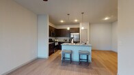 This single-story unit in Buda, Texas, presents a well-designed open-concept layout with consistent wood-look flooring and neutral gray-toned walls throughout. The kitchen serves as a central focal point, outfitted with rich dark espresso cabinetry, granite-style countertops, and a full suite of stainless steel appliances including a range, microwave, and French door refrigerator. A kitchen island with a built-in sink and seating for two is highlighted by pendant lighting above, creating a functional and inviting space that flows seamlessly into the living area, which features a ceiling fan and natural light from a nearby window.

The bedrooms are generously proportioned, each equipped with ceiling fans and wood-look flooring. Notable among them are walk-in closets with built-in shelving and hanging rods, providing ample storage. One bedroom offers an en-suite bathroom access, while the bathrooms throughout feature dark cabinetry, granite-topped vanities, tub-shower combinations with white tile surrounds, and durable wood-look flooring. The overall design maintains a clean, contemporary aesthetic with a cohesive palette of dark cabinetry contrasted against white and light gray surfaces.
