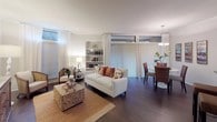 This single-floor residence is thoughtfully designed with an open-concept layout that connects the living and dining areas seamlessly. The living room features dark hardwood flooring, sheer white floor-to-ceiling curtains, and large windows that invite natural light and outdoor views. A built-in white bookshelf serves as a functional focal point, while vertical blinds along the exterior wall provide adjustable light control. The dining area is defined by a round white table, woven chairs, and a classic chandelier overhead, with large windows enhancing the bright, airy ambiance.

The kitchen is equipped with warm oak cabinetry, granite countertops, and stainless steel appliances including a gas range and built-in microwave. The bedroom is a calm, well-proportioned retreat with multiple windows fitted with blinds, a closet, and neutral tones throughout.

Two bathrooms serve the residence. One features a granite vanity, white cabinetry, and a tub-shower combination, while the primary bathroom offers a separate glass-enclosed shower, a granite double vanity with a built-in vanity seat, and a large mirror — both finished with hardwood-style flooring.