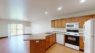 Located at 420 College Avenue in De Pere, Wisconsin, this one-bedroom, one-bathroom unit offers a functional and comfortable single-floor layout. The kitchen serves as the heart of the space, featuring warm oak cabinetry, a peninsula with a stainless steel sink and laminate countertops, and a full suite of white appliances including a refrigerator, electric range, microwave, and dishwasher. Recessed lighting illuminates the kitchen and adjoining living area, which flows naturally from the entry door. Wood-look vinyl flooring runs throughout the main living and kitchen areas, adding a clean, durable finish. The bedroom is a comfortable size, bathed in natural light from a window with outdoor views, and features blue tile-pattern carpeting and a wall-mounted air conditioning unit alongside baseboard heating. A dedicated walk-in closet with wire shelving provides ample storage. The bathroom is finished with matching wood-look flooring, a warm-toned vanity, and a full tub-shower combination with a curtain rod. Neutral wall tones and straightforward design choices create a clean, practical atmosphere throughout, making this an efficient and livable space.