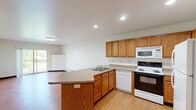 Located at 420 College Avenue in De Pere, Wisconsin, this one-bedroom, one-bathroom unit offers a functional and comfortable single-floor layout. The kitchen serves as the heart of the space, featuring warm oak cabinetry, a peninsula with a stainless steel sink and laminate countertops, and a full suite of white appliances including a refrigerator, electric range, microwave, and dishwasher. Recessed lighting illuminates the kitchen and adjoining living area, which flows naturally from the entry door. Wood-look vinyl flooring runs throughout the main living and kitchen areas, adding a clean, durable finish. The bedroom is a comfortable size, bathed in natural light from a window with outdoor views, and features blue tile-pattern carpeting and a wall-mounted air conditioning unit alongside baseboard heating. A dedicated walk-in closet with wire shelving provides ample storage. The bathroom is finished with matching wood-look flooring, a warm-toned vanity, and a full tub-shower combination with a curtain rod. Neutral wall tones and straightforward design choices create a clean, practical atmosphere throughout, making this an efficient and livable space.