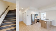 Located at 99 Milford Ave in Waterloo, Ontario, this thoughtfully designed two-storey unit offers three bedrooms and two bathrooms across two well-proportioned floors. The main level features an open-concept kitchen and living area bathed in natural light from large windows. The kitchen is appointed with stainless steel appliances, a stainless electric range, refrigerator, and microwave, complemented by a wood-accented island with a white quartz countertop and an undermount sink, white upper cabinetry, and light wood lower cabinets. Light-toned luxury vinyl plank flooring flows throughout both levels, lending a clean, cohesive aesthetic. A staircase with dark-toned treads connects the two floors. The upper level hosts the bedrooms, including a primary bedroom with sliding glass door access to a private balcony overlooking the neighbourhood. Additional bedrooms are bright and airy, each with windows providing natural light. The two bathrooms are finished in a neutral palette, one featuring a soaker tub with large-format stone-look tile surround, and the other a vanity with wood cabinetry and a white quartz countertop. Recessed lighting throughout adds a polished, contemporary feel to this well-appointed Waterloo residence.