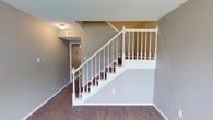 Located at 5201 Monaco Dr in Pascagoula, Mississippi, this two-story home offers a straightforward and functional layout designed for comfortable everyday living. The interior is finished with plush carpeting throughout the main living areas, providing warmth and comfort underfoot. A classic staircase with crisp white balusters, turned newel posts, and dark wood treads serves as a central architectural feature, connecting the two floors with a clean, traditional aesthetic. The neutral gray wall tones carry throughout the space, creating a cohesive and calm interior palette that pairs well with the light-colored trim and baseboards. The textured ceiling adds depth and dimension to the rooms, while flush-mount ceiling lighting provides consistent illumination. A visible HVAC vent integrated into the ceiling reflects practical climate control throughout the home. The lower level opens to a hallway that leads further into the home's interior, hinting at additional rooms and living spaces beyond the main stairwell area. Overall, the home presents a tidy, move-in ready appearance with a classic design sensibility, making it a solid and dependable residence in the Pascagoula community.