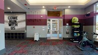 This single-floor fitness center is thoughtfully designed to support a complete workout experience. The space is immediately recognizable by its distinctive tri-tone wall design, featuring alternating bands of burgundy, gray, and charcoal that lend the facility a bold, energetic atmosphere throughout.

The main cardio area is a standout feature, lined with multiple treadmills and elliptical machines, each equipped with individual screens for entertainment during workouts. Large windows along the cardio wall flood the space with natural light and offer views of the surrounding outdoor landscape. Full-length mirrors on adjacent walls visually expand the room and assist with form checks during exercise.

A dedicated spin and functional training area houses stationary cycling bikes alongside a well-stocked rack of medicine balls, stability balls, and resistance equipment, catering to a variety of training styles. Wall hooks near the entrance provide convenient storage for jump ropes and resistance bands.

The facility also includes a separate package locker room, lined floor-to-ceiling with secure parcel lockers and featuring its own exterior access door—a practical amenity for residents. Patterned carpet tiles in muted red and gray tones anchor each zone of the facility, tying the design together cohesively. Recessed lighting throughout ensures consistent illumination across all areas of the space.