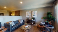 Located at 3855 SW Murray Blvd in Beaverton, Oregon, this single-floor residence offers a thoughtfully arranged layout with a cohesive, nature-inspired aesthetic throughout. The living area serves as the heart of the space, featuring neutral-toned walls, recessed lighting, and a distinctive textured bamboo accent wall that adds warmth and visual depth. A glass-top coffee table with a natural wood base anchors the seating area alongside a tufted leather sofa and leather accent chair, creating an inviting, well-curated atmosphere.

The kitchen is outfitted with dark wood cabinetry, stainless steel appliances, and light flooring, offering a clean, contemporary look. A sliding glass door adjacent to the kitchen allows natural light to filter in and provides outdoor views of the surrounding Beaverton area.

The bedroom is a comfortable retreat featuring plush carpeting, a built-in desk area with a decorative oval shelving unit, and the same bamboo accent wall detail seen in the living room, creating a unified design language. The hallway connecting the rooms features light hardwood-style flooring and subtle wall décor.

The bathroom is finished with a dark wood vanity, white countertop, large mirror, and light tile flooring, maintaining the modern, earthy tone found throughout the entire space.