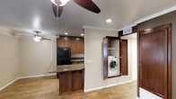 This single-floor residence offers a well-designed open-concept layout that seamlessly connects the kitchen and living areas, creating a cohesive and functional living environment. The kitchen is outfitted with warm-toned wood cabinetry that provides generous storage, granite countertops, and a breakfast bar peninsula that serves as both a prep space and casual dining area. A black refrigerator anchors the kitchen, complementing the rich wood tones throughout. Recessed lighting illuminates the space efficiently, while crown molding along the ceiling adds a refined architectural touch. Durable wood-look flooring extends throughout, offering both practicality and visual warmth. A ceiling fan enhances air circulation in the main living area, contributing to everyday comfort. One of the standout functional features is the in-unit laundry closet, discreetly housed behind full bi-fold wood panel doors that blend seamlessly with the surrounding millwork — a practical addition that keeps laundry conveniences neatly out of sight. The neutral wall tones and clean finishes throughout give the space a bright, approachable ambiance that is easy to personalize.