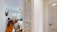 Located at 1100 N La Salle Blvd in Chicago's sought-after Gold Coast neighborhood, this efficiently designed one-bedroom, one-bathroom unit offers a well-organized layout across a single floor. The spacious bedroom serves as the heart of the unit, featuring warm parquet hardwood flooring, bright white walls, and a ceiling fan that enhances air circulation. Natural light fills the room through windows offering views of the surrounding cityscape, while a wall-mounted TV and built-in dresser with cabinet storage add practical convenience. A closet with double doors provides ample storage. The bedroom comfortably accommodates a sleeping area alongside a dedicated workspace and sitting area. The bathroom is a standout feature, finished with elegant marble-look tile flooring and wall surround in the walk-in shower, complemented by a sleek modern vanity with wood-toned cabinetry and a crisp white countertop. A hallway connects the main living spaces and provides access to the dedicated laundry area, adding everyday convenience. The overall ambiance is clean, bright, and functional, blending classic Chicago building character — evident in the parquet floors and radiator heating — with updated, contemporary finishes throughout.