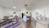 This single-floor residence is thoughtfully designed with a bright, open-concept layout and consistent wood-look flooring throughout. The welcoming entryway features a smart thermostat panel and built-in wall organizers, setting a functional tone from the start. The living room serves as the heart of the home, anchored by a striking stone-surround fireplace and sliding glass doors that open to a private balcony, filling the space with natural light and outdoor views. Adjacent to the living area, a dedicated dining space accommodates a full table and benefits from its own window overlooking the exterior. The kitchen is efficiently designed with white cabinetry, a tile backsplash, black appliances, and a peninsula island with bar seating — ideal for casual dining or entertaining. A pass-through layout connects the kitchen seamlessly to the dining and living areas. The primary bedroom is generously sized, featuring dual windows, a ceiling fan, and direct access to a spacious walk-in closet with built-in wire shelving. A second bedroom also includes a ceiling fan and natural light. The bathroom is finished with granite-style countertops, white shaker cabinetry, and a tub-shower combination. Throughout, the textured ceilings and crisp white walls create a clean, cohesive aesthetic.
