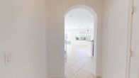 This two-story home showcases a bright, clean aesthetic with a neutral color palette and thoughtful architectural details throughout. The main level is anchored by light-toned ceramic tile flooring and features a graceful arched entryway that opens into a spacious living and dining area, filled with natural light from large windows overlooking the outdoors. A well-designed kitchen sits at the heart of the home, equipped with rich cherry wood cabinetry, granite countertops, a breakfast bar peninsula, recessed lighting, and white appliances including a range, over-the-range microwave, refrigerator, and dishwasher. A staircase with white-painted balustrades and carpeted treads leads to the upper level. A powder bathroom on the main floor features matching cherry wood vanity cabinetry and a charming oval window. The upper level hosts multiple bedrooms, each with plush wall-to-wall carpeting and windows that bring in ample natural light. The primary bathroom is generously sized, offering dual vanities with warm wood cabinetry, a soaking tub, a separate glass-enclosed shower, and large mirrors illuminated by a Hollywood-style light bar. Throughout, the home presents a clean, move-in-ready environment with a consistent and cohesive design language.