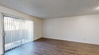 This single-floor unit offers a practical and well-organized layout with consistent neutral tones and clean finishes throughout. The living area is a generous, open space featuring dark wood-style laminate flooring and a textured ceiling. A large sliding glass door with vertical blinds allows abundant natural light to fill the room while providing outdoor access. The entry area shares the same laminate flooring, creating a seamless transition into the main living space.

The kitchen is efficiently designed with white cabinetry, light-toned countertops, and a peninsula that offers additional prep space and separates the kitchen from the living area. Black appliances, including a refrigerator, range, and dishwasher, complement the white cabinetry. A double stainless steel sink sits beneath a window, adding natural light to the workspace.

The bedrooms are carpeted and well-lit, each featuring vertical blinds over windows that allow controlled natural light. The textured ceilings carry throughout these rooms, maintaining a cohesive aesthetic.

The bathrooms are clean and functional. One features a full tub-shower combo with white surround, while another includes a wide vanity with dual sinks, ample white cabinetry, a large mirror, and hardwood-style flooring, offering a practical and organized space.
