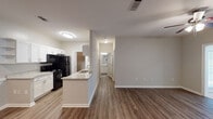 This single-story residence in Spanish Fort, Alabama offers a thoughtfully designed open-concept layout with a cohesive blend of modern finishes and functional living spaces. Warm-toned wood-look vinyl plank flooring flows throughout the main living areas, complemented by neutral gray walls and crisp white trim that create a clean, inviting atmosphere.

The kitchen serves as a central feature of the home, designed in a galley style with ample white shaker cabinetry, granite-look countertops, and a full suite of black appliances including a range, microwave, refrigerator, and dishwasher. A double-basin stainless steel sink anchors one side, while a peninsula with additional counter space opens toward the living area, enhancing the open flow of the layout.

The living room is spacious and well-lit, featuring a ceiling fan with integrated lighting, a large window that admits natural light, and direct access to the entry door. The bedroom is carpeted for comfort and includes a ceiling fan, a walk-in closet, and sliding glass doors that open to an outdoor area.

The bathroom is finished with granite-top vanity, wood-look flooring, and a full tub-shower combination with tiled surround and brushed nickel fixtures. A dedicated laundry area is accessible from the kitchen corridor, adding everyday convenience to this well-rounded home.