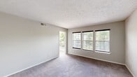 This efficiently designed 2-bedroom, 1-bathroom unit is laid out across a single floor, offering a functional and cohesive living environment. The combined kitchen and living room forms the heart of the space, with the kitchen featuring granite countertops, white shaker-style cabinetry, wood-look luxury vinyl flooring, and black stainless steel appliances including a refrigerator, range, and built-in microwave. Neutral gray walls and a textured ceiling carry throughout the unit, creating a consistent and understated aesthetic.

The living room is bright and open, benefiting from a bank of three windows with exterior views of surrounding greenery, as well as direct access to a private balcony through a sliding glass door—bringing in natural light and outdoor connection. Soft wall-to-wall carpeting extends through the living area and both bedrooms.

The primary bedroom is a comfortable size, offering a walk-in closet with built-in shelving for organized storage. The second bedroom also features carpeting and neutral walls. The shared bathroom is well-appointed with granite countertops, a framed vanity mirror, gray cabinetry with brushed gold hardware, wood-look flooring, and a tiled tub-shower combination. A hallway connects the rooms, completing this practical and neatly arranged layout.