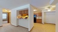 This single-floor residence offers a practical and comfortable layout designed for everyday living. The open-concept living area is finished with neutral wall-to-wall carpeting and warm wood baseboards, creating a cohesive and inviting atmosphere throughout. A ceiling fan adds both function and character to the living space, which flows seamlessly toward the bedroom wing.

The kitchen is a standout functional hub, featuring abundant oak cabinetry that provides generous storage above and below. A full suite of black appliances includes a range with coil burners, a dishwasher, and a full-size refrigerator. Light-toned countertops and tile flooring complete the kitchen's clean, utilitarian aesthetic. A pass-through counter opening connects the kitchen to the living area, enhancing the open feel and making the space ideal for casual interaction.

The bedrooms are well-sized, each with plush carpeting, natural light from large windows, baseboard heating, and closet space. The entry bedroom also features a dedicated entryway door with additional storage.

Two bathrooms serve the unit — one with a vanity, oak cabinetry, and a tub/shower combination, and another with a single vanity and toilet. Both feature tile flooring and are finished with consistent warm wood trim throughout, tying the overall design of the residence together cohesively.