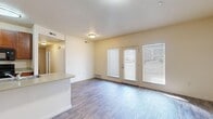 This single-story, 4-bedroom, 2-bathroom home offers a practical and comfortable layout designed to maximize functionality. The open-concept living room and kitchen area serves as the heart of the home, featuring durable wood-style flooring, neutral warm-toned walls, and a textured ceiling. The living room receives generous natural light through a set of large windows and a glass-panel door fitted with blinds, creating a bright and welcoming atmosphere. A peninsula counter with an integrated sink connects the kitchen to the living space, offering a convenient casual dining or prep area. The kitchen is equipped with warm wood cabinetry, light countertops, and a full suite of black appliances including a refrigerator, electric range, built-in microwave, and dishwasher. The four bedrooms feature plush carpeting and windows with blinds, providing a cozy and private retreat. Sliding double doors lead to closet space in at least one of the bedrooms, adding practical storage. The two bathrooms are finished with wood-style tile flooring, granite-look vanity countertops, and full tub-shower combinations with clean white surrounds. A hallway connects the bedrooms and bathrooms, completing the efficient floor plan of this well-appointed home.