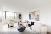 Located at 99 Gorge Rd in Edgewater, NJ, this well-appointed two-bedroom, one-bathroom residence offers a thoughtfully designed single-floor layout with a clean, modern aesthetic throughout. Light hardwood flooring flows seamlessly across the living, dining, and bedroom areas, creating a cohesive and inviting atmosphere.

The open living and dining area is bathed in natural light from large windows overlooking lush greenery, with the living room featuring a wall-mounted TV, contemporary furnishings, and a geometric coffee table. The adjacent dining space is elevated by a striking brass sputnik chandelier and a round dark wood table set beneath a large window with outdoor views.

The galley-style kitchen is efficiently designed with white shaker cabinetry, white quartz countertops, a subway tile backsplash, and a full suite of stainless steel appliances including a refrigerator, range, microwave, and dishwasher.

Both bedrooms are bright and serene, each featuring large windows with verdant views, hardwood floors, and a calm neutral palette. The primary bedroom includes a wall-mounted TV and a cozy accent chair.

The bathroom is finished with warm stone tile floors, a tub-shower combo with stone surround, a mid-century walnut vanity, and recessed lighting. A clean hallway connects the private areas of the residence, completing this well-organized and stylish home.