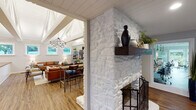 Located in Anderson, SC, this thoughtfully designed single-floor space blends modern aesthetics with warm, inviting character throughout. The centerpiece of the main living area is a striking white-painted stone fireplace with a rich wood mantel, anchoring the room with rustic charm. Soaring vaulted ceilings with exposed white-painted beams and shiplap detailing amplify the sense of openness, while a dramatic circular chandelier with Edison-style bulbs adds an industrial-modern touch. Large windows flood the living area with natural light and frame views of the surrounding greenery.

The kitchen is a standout, featuring a generous island with a warm wood butcher block countertop, a gold-toned faucet, white cabinetry, stainless steel appliances, and open wood shelving set against a bold geometric-patterned accent wall with a sleek range hood as its focal point.

A dedicated office area connects seamlessly to the rest of the space, offering built-in granite-top workstations, pendant lighting, and floor-to-ceiling windows and sliding glass doors that open to a well-maintained outdoor landscape. Durable wood-look flooring runs throughout, unifying the various functional zones. The overall ambiance is modern, clean, and professionally curated, making the space equally suited for productivity and comfort.