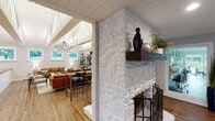 Located in Anderson, SC, this thoughtfully designed single-floor space blends modern aesthetics with warm, inviting character throughout. The centerpiece of the main living area is a striking white-painted stone fireplace with a rich wood mantel, anchoring the room with rustic charm. Soaring vaulted ceilings with exposed white-painted beams and shiplap detailing amplify the sense of openness, while a dramatic circular chandelier with Edison-style bulbs adds an industrial-modern touch. Large windows flood the living area with natural light and frame views of the surrounding greenery.

The kitchen is a standout, featuring a generous island with a warm wood butcher block countertop, a gold-toned faucet, white cabinetry, stainless steel appliances, and open wood shelving set against a bold geometric-patterned accent wall with a sleek range hood as its focal point.

A dedicated office area connects seamlessly to the rest of the space, offering built-in granite-top workstations, pendant lighting, and floor-to-ceiling windows and sliding glass doors that open to a well-maintained outdoor landscape. Durable wood-look flooring runs throughout, unifying the various functional zones. The overall ambiance is modern, clean, and professionally curated, making the space equally suited for productivity and comfort.