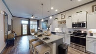 Located in Smyrna, TN, this single-floor residence offers a thoughtfully designed open-concept layout that seamlessly connects the kitchen, dining, and living areas. The kitchen is a standout feature, equipped with crisp white shaker cabinetry, stainless steel appliances, subway tile backsplash, granite countertops, and a central island with bar seating illuminated by stylish pendant lighting. Rich hardwood-style flooring flows throughout the main living areas, complemented by bold crown molding and recessed lighting.

The living room is bright and welcoming, with large windows dressed in floor-to-ceiling drapes that invite natural light while offering a cozy reading nook with views to the outdoors. A ceiling fan adds both function and charm to the space.

The primary bedroom features plush carpeting, generous proportions, access to a walk-in closet, and an en suite bathroom. The bathroom is finished with granite countertops, undermount sinks, wood-style flooring, and a glass-enclosed walk-in shower. A second bedroom also offers carpet, large windows with outdoor views, and ample natural light. Throughout the residence, gray-toned interior doors and neutral warm walls create a cohesive, modern aesthetic.