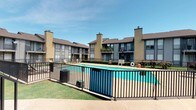 This residential community is defined by its classic brick construction and thoughtfully designed outdoor amenities. The centerpiece of the property is a generously sized outdoor swimming pool with clear, blue-green water, surrounded by a spacious concrete pool deck furnished with lounge chairs — ideal for relaxing on sunny days. The pool area is enclosed by a sturdy iron fence, providing both safety and a sense of structure to the outdoor space.

The multi-story buildings feature a warm, tan brick exterior paired with brown-trimmed balconies and large windows that allow natural light into each unit. Many balconies display personal touches such as potted plants and décor, adding character to the façade. Prominent brick chimneys rise above the roofline, complementing the traditional architectural style with brown pitched roofs.

Lush green lawn areas border the pool courtyard, contributing to the community's inviting atmosphere. The layout of the buildings creates an enclosed, community-oriented feel around the pool area, fostering a sense of neighborly connection. Under expansive blue skies, the outdoor common areas offer residents a comfortable and attractive retreat that enhances everyday living.