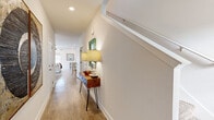 This two-story home is thoughtfully laid out across two floors, with the main level housing the primary living areas and the upper level offering additional private spaces. The ground floor features an open-concept kitchen and living room, where white cabinetry, granite countertops, a breakfast bar with seating, and stainless steel appliances define the kitchen. The living area flows seamlessly from the kitchen, highlighted by a ceiling fan, recessed lighting, and multiple windows that invite generous natural light and outdoor views. Hardwood-style flooring runs consistently throughout both levels, contributing to a cohesive, clean aesthetic. A welcoming hallway on the main level, accented by a staircase with a sleek railing, connects the entry to the living spaces. The upper floor contains three bedrooms, including a well-proportioned primary suite with multiple windows, a ceiling fan, an en-suite bathroom with a walk-in shower, and an adjacent closet with built-in shelving. Additional bathrooms include a full tub-shower combination. A dedicated office with a window provides a bright, functional workspace. The overall ambiance is light, neutral, and calm throughout.