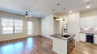 Located in Grapevine, TX, this single-story, one-bedroom, one-bathroom residence offers a well-designed open-concept layout with modern finishes throughout. The combined kitchen and living area serves as the heart of the home, showcasing warm wood-style flooring, neutral tones, and a ceiling fan that enhances comfort. A sliding glass door fills the living space with natural light and provides outdoor access.

The kitchen is a standout feature, centered around a peninsula island with a dark granite countertop, an undermount sink, and matte black fixtures. Tall white shaker-style cabinetry with glass-front upper panels provides generous storage, while a classic subway tile backsplash and stainless steel appliances—including a range, microwave, and refrigerator—complete the contemporary look. Stylish gold pendant lights illuminate the island from above.

The spacious primary bedroom features plush carpet flooring and direct access to the full bathroom, which is appointed with a granite-topped vanity, white cabinetry, a soaking tub and shower combination, and wood-style flooring.

A dedicated laundry room houses a full-size top-loading washer and dryer alongside built-in shelving for added storage. A hallway connects the rooms, rounding out a functional and cohesive floor plan.