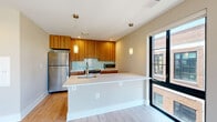 Located at 713 Lamont St NW in Washington, DC's vibrant Columbia Heights neighborhood, this thoughtfully designed one-bedroom, one-bathroom residence offers a well-appointed single-floor layout. Light hardwood flooring flows throughout the unit, complementing warm neutral walls and crisp white trim for a clean, modern aesthetic.

The living room is a bright, open space anchored by large floor-to-ceiling windows and a sliding glass door that frames sweeping views of the surrounding DC cityscape and tree canopy, flooding the room with abundant natural light. Track lighting adds functional illumination overhead.

The contemporary kitchen is a standout feature, showcasing rich wood-grain cabinetry extending to the ceiling, a teal glass tile backsplash, stainless steel appliances — including a full-size refrigerator, range, and microwave — and a sleek white peninsula with an undermount sink and pendant lighting above. A large window beside the peninsula brings in additional natural light.

The bedroom offers a comfortable, quiet retreat with its own large window overlooking the neighborhood's treetops. A dedicated closet with built-in wire shelving provides organized storage. The bathroom includes a full soaking tub with tiled surround, a vanity with wood cabinetry, and tile flooring. An additional closet in the hallway offers supplemental storage.