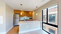 Located at 713 Lamont St NW in Washington, DC's vibrant Columbia Heights neighborhood, this thoughtfully designed one-bedroom, one-bathroom residence offers a well-appointed single-floor layout. Light hardwood flooring flows throughout the unit, complementing warm neutral walls and crisp white trim for a clean, modern aesthetic.

The living room is a bright, open space anchored by large floor-to-ceiling windows and a sliding glass door that frames sweeping views of the surrounding DC cityscape and tree canopy, flooding the room with abundant natural light. Track lighting adds functional illumination overhead.

The contemporary kitchen is a standout feature, showcasing rich wood-grain cabinetry extending to the ceiling, a teal glass tile backsplash, stainless steel appliances — including a full-size refrigerator, range, and microwave — and a sleek white peninsula with an undermount sink and pendant lighting above. A large window beside the peninsula brings in additional natural light.

The bedroom offers a comfortable, quiet retreat with its own large window overlooking the neighborhood's treetops. A dedicated closet with built-in wire shelving provides organized storage. The bathroom includes a full soaking tub with tiled surround, a vanity with wood cabinetry, and tile flooring. An additional closet in the hallway offers supplemental storage.